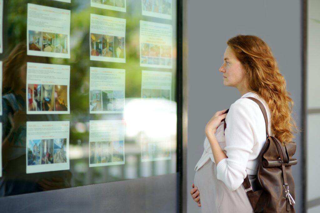 Real Estate Investment Essentials for Beginners | In-depth Guide 1 Young pregnant woman exploring storefront of real estate agency.